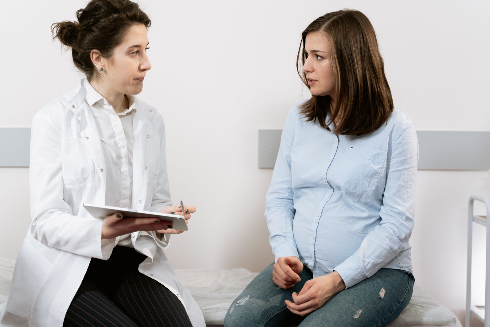 Free A doctor consults with a pregnant patient discussing healthcare options in a medical facility. Stock Photo.