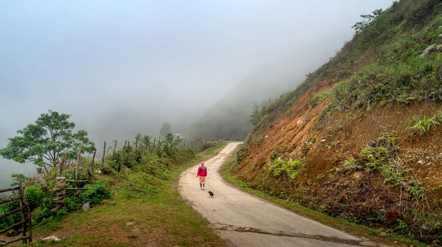 Chemin de terre longeant un flanc de montagne dans la brume