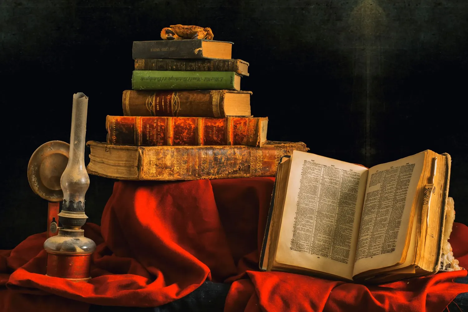 Pile de livres anciens et lampe à huile sur un drapé rouge
